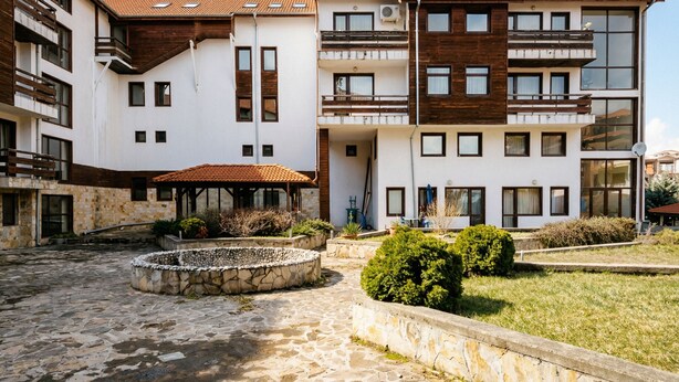 Ein mehrstöckiges Gebäude mit Innenhof, der einen Steinfountain, Pflanzgefäße und eine Holzpergola zeigt.