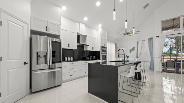 Una cucina moderna con elettrodomestici in acciaio inossidabile, mobili bianchi e un angolo bar con sgabelli.