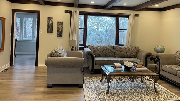 Un salon comprenant un canapé, un fauteuil et une table basse, avec un plancher en bois et une vue dégagée grâce à de grandes fenêtres.