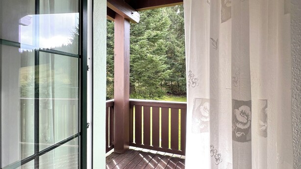 A room with a sliding glass door leading to an outdoor deck with a wooden railing. - Cozy vacation apartment "Talblick" in Eibenstock, district Carlsfeld (Eibenstock)