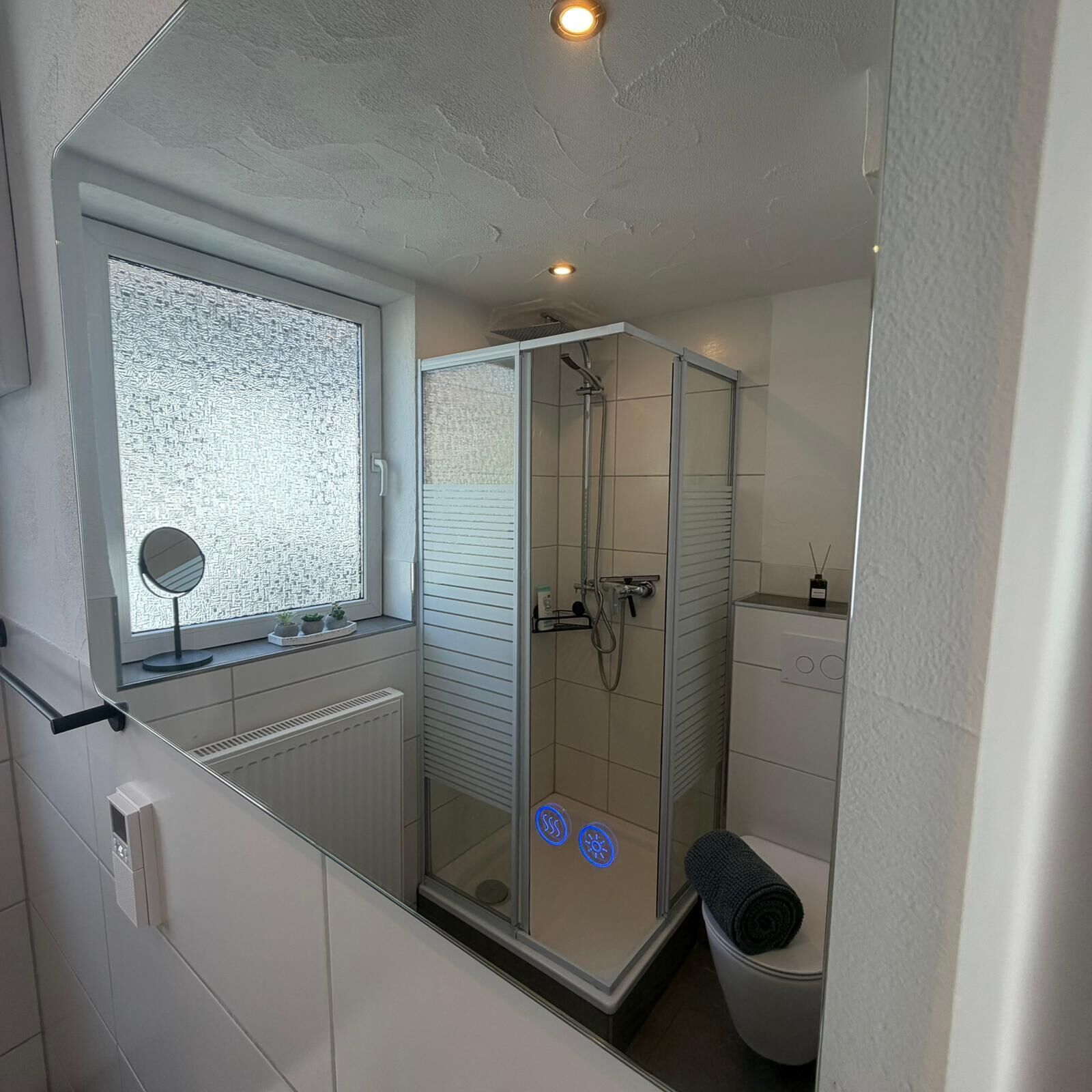 A modern bathroom with a glass shower enclosure, a toilet, and a window with frosted glass.