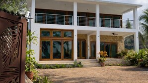 A two-story modern house with a covered patio, large windows, and a gravel driveway. - Casa Parota Suite Conacaste (Higuera Blanca)
