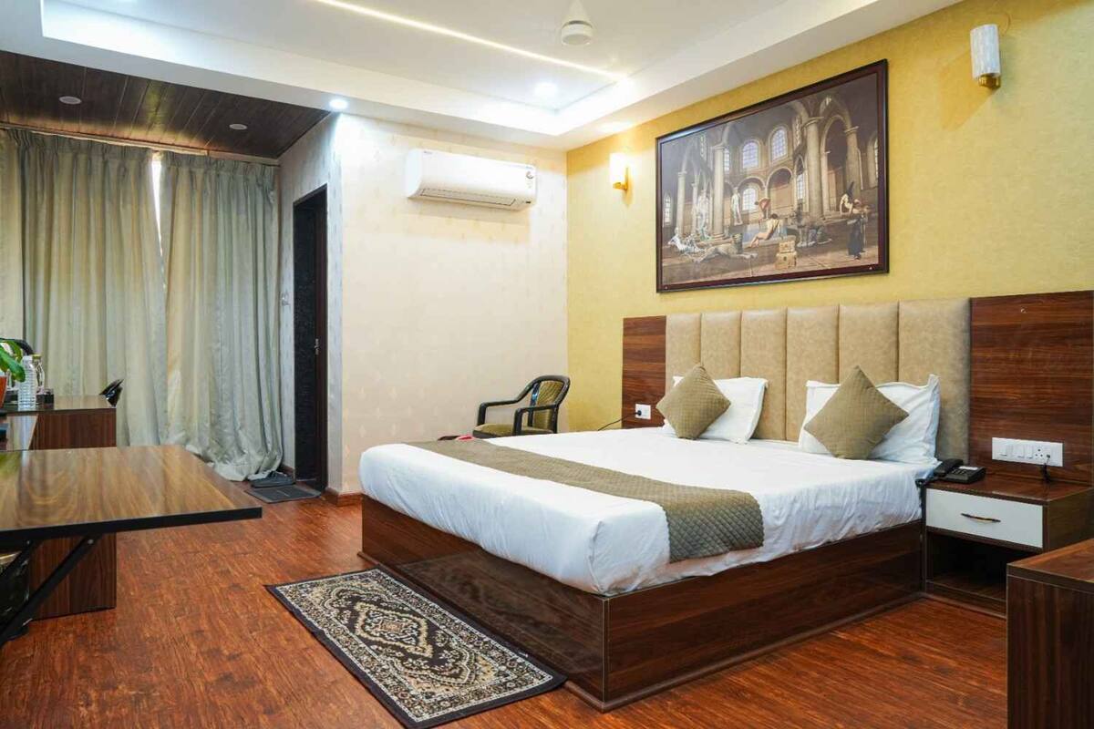 A hotel room with a large bed, a desk, a chair, and a painting on the wall.