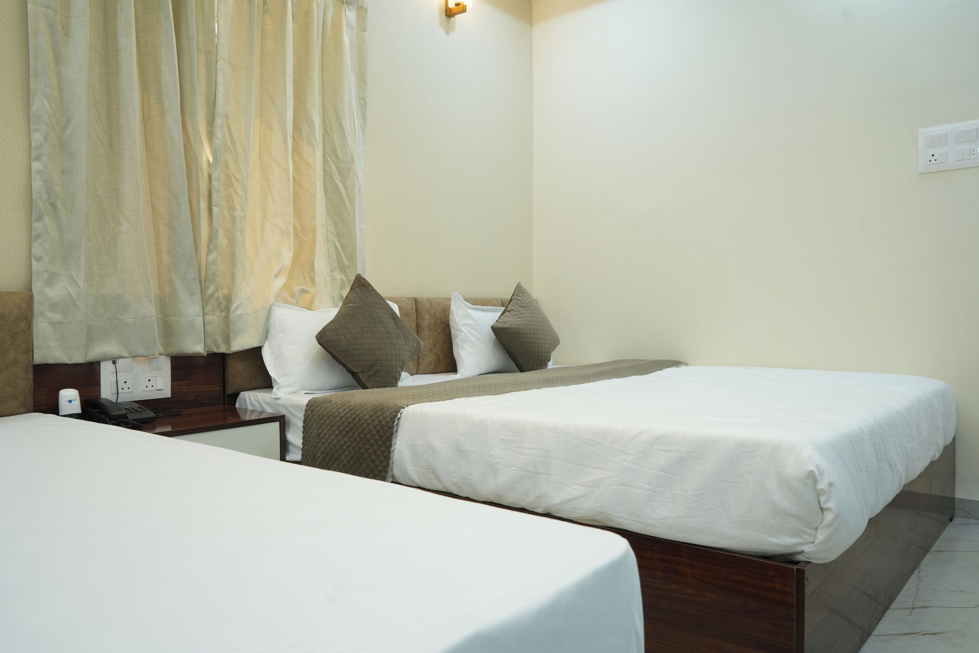 Une chambre d’hôtel avec deux lits, une table de chevet avec un téléphone, une prise électrique au mur et un rideau.