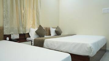 A hotel room with two beds, a bedside table with a phone, a wall socket, and a curtain.