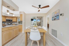 A modern kitchen with wooden cabinets, a dining table, and ceiling fans. - Canal-Front 3BR w/ Heated Saltwater Pool, Dock, BBQ & Ping-Pong — Near Beaches! (Port Charlotte)