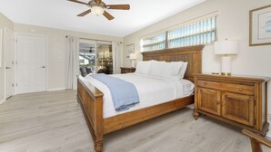 Een slaapkamer met een houten bed, een plafondventilator, een nachtkastje, een dressoir en een raam met jaloezieën.