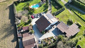 Vista aérea de una propiedad residencial con piscina, varios autos y un jardín bien cuidado.