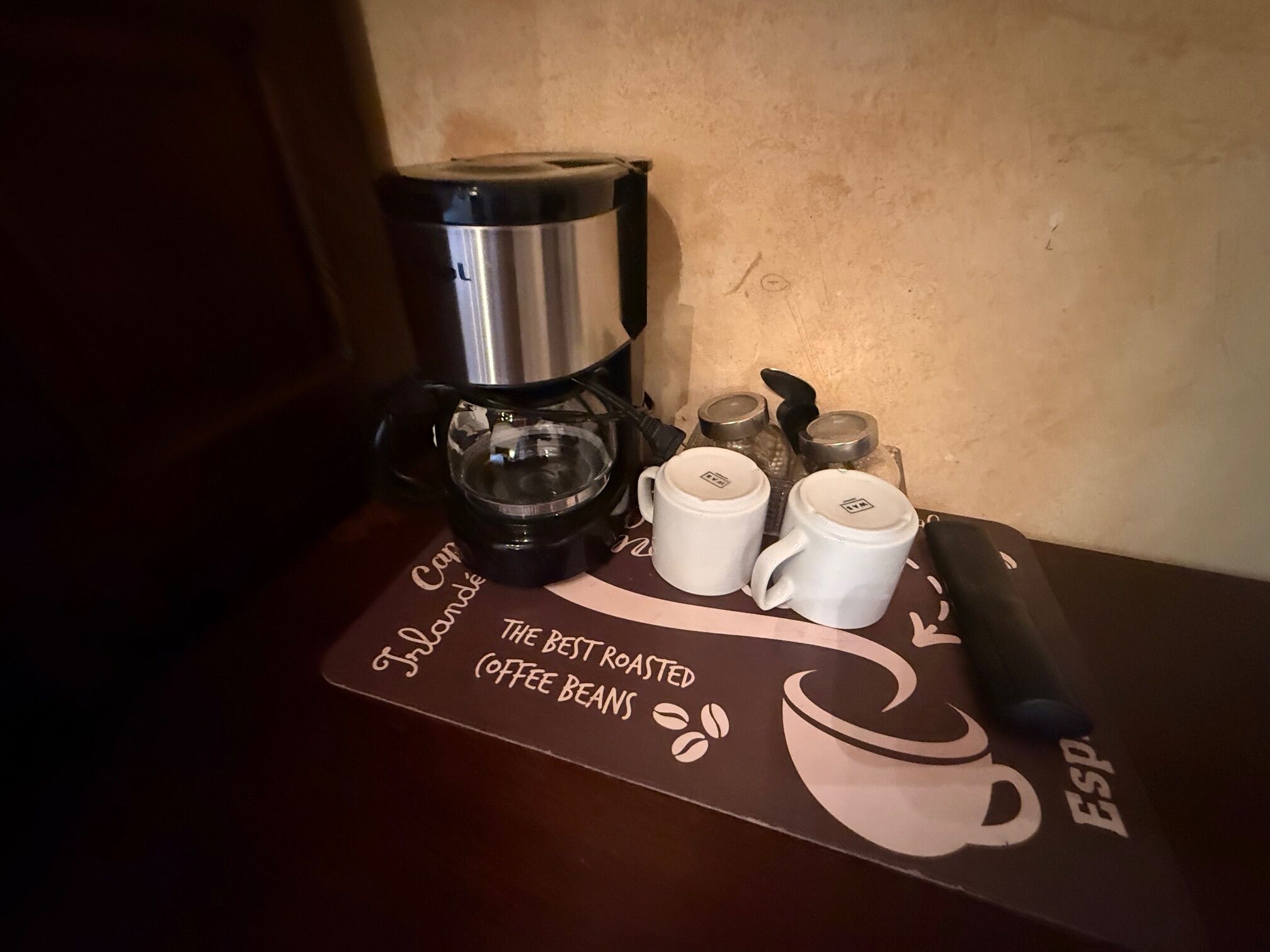 Une machine à café, deux tasses blanches et un porte-capsules à café sont posés sur une table recouverte d’un set de table sur le thème du café.