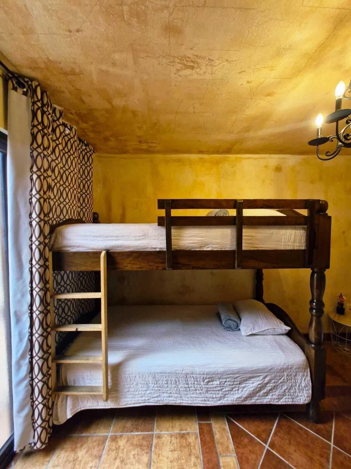 Una cama individual superpuesta con escalera, una mesita pequeña y una cortina estampada.