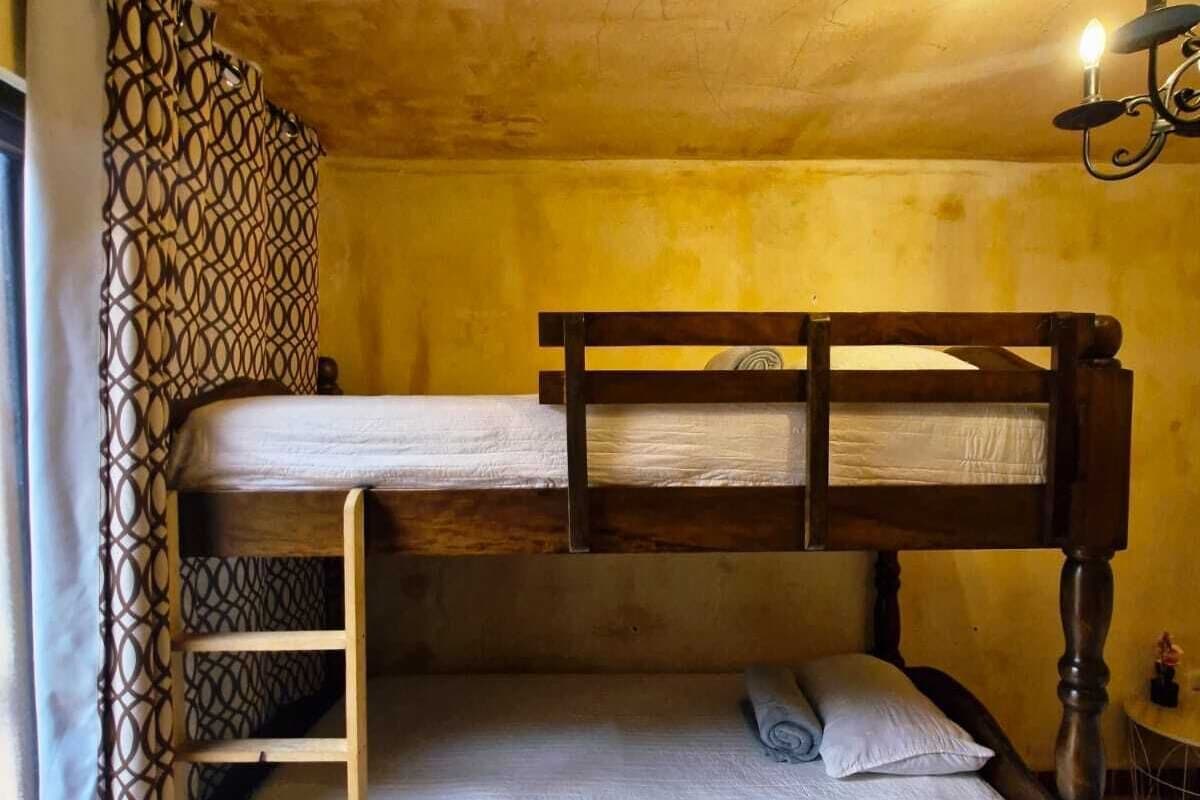 Una cama individual superpuesta con escalera, una mesita pequeña y una cortina estampada.