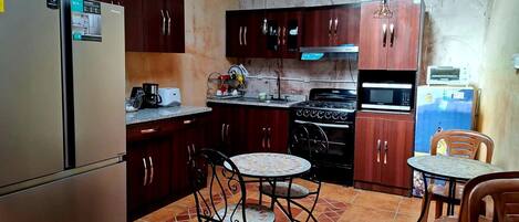 A compact kitchen with a refrigerator, stove, microwave, and dining area with two chairs and a small table.