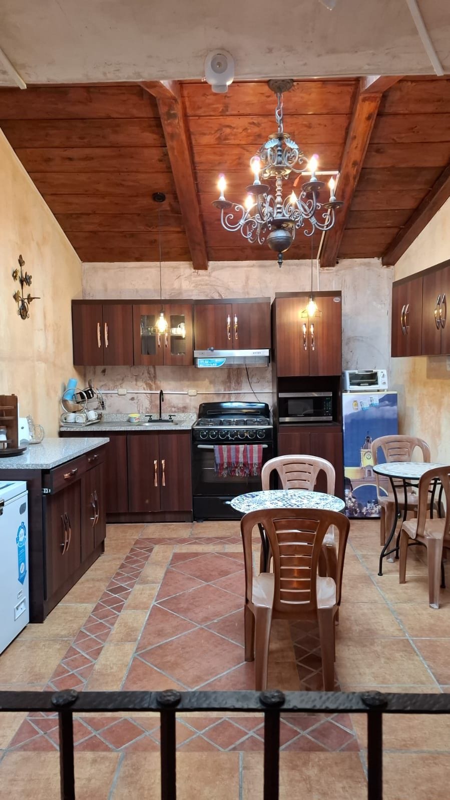Een keuken met houten kastjes, een gasfornuis, een magnetron en een eethoek met een tafel en stoelen.