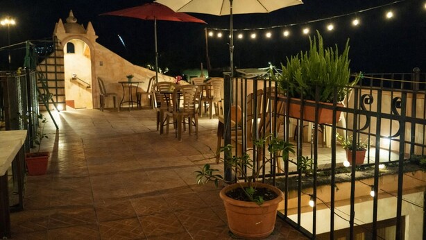 Une terrasse extérieure avec des tables et des chaises, des plantes en pot et des guirlandes lumineuses.