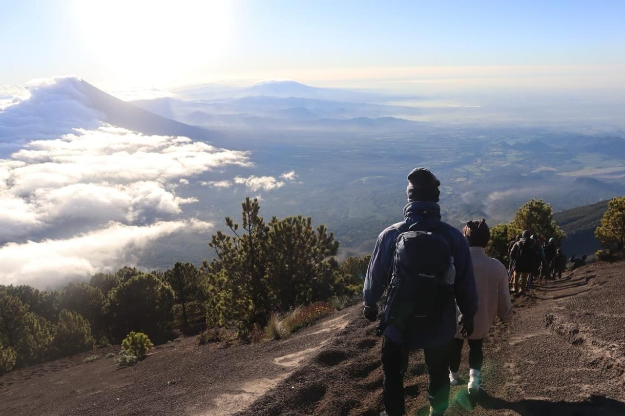 A mountainous landscape with a clear sky, a hiker in the foreground, and a distant mountain range.