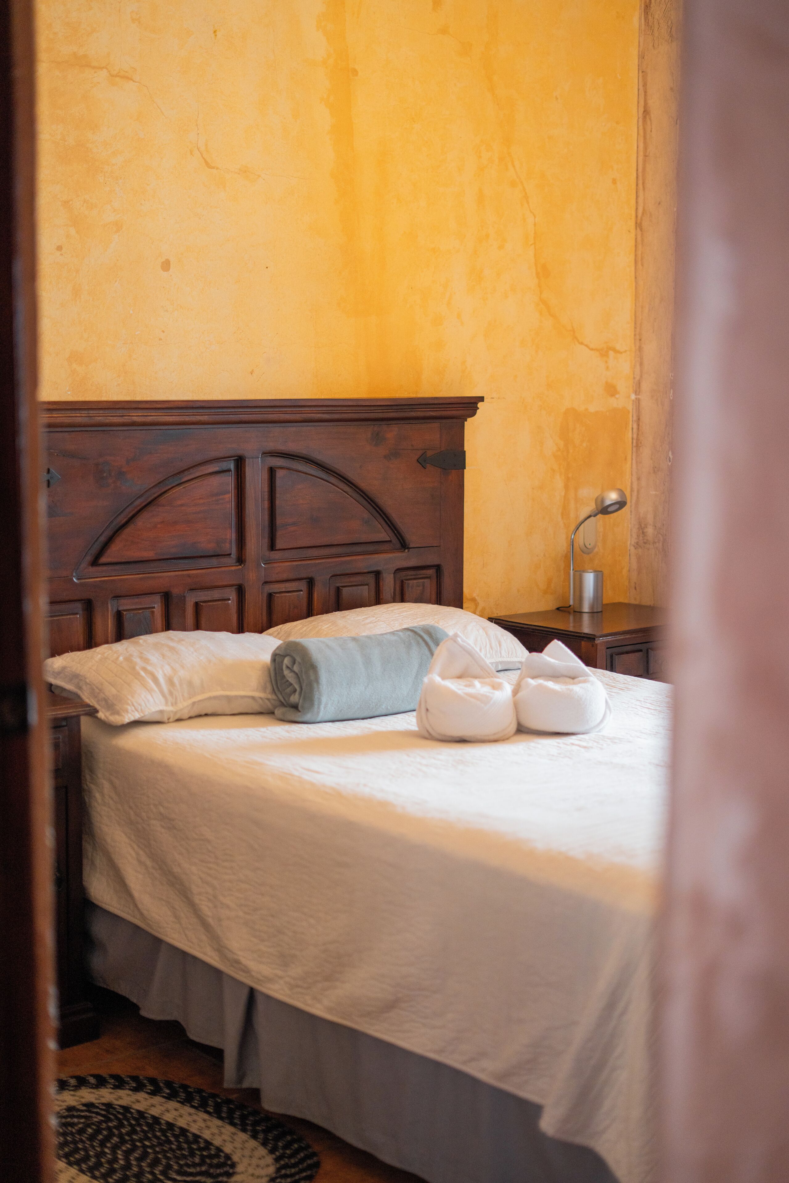 A bed with a wooden headboard, a white bedspread, and rolled towels.