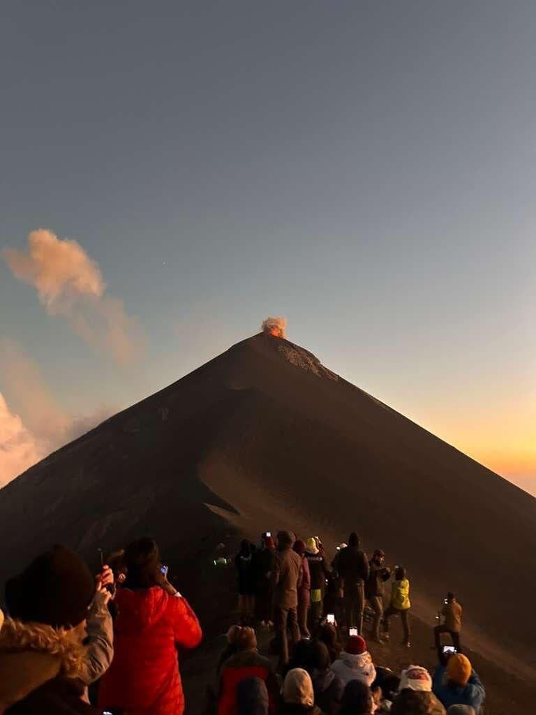 Une foule de personnes se trouve au pied d’une montagne, vraisemblablement un volcan, sous un ciel dégagé.