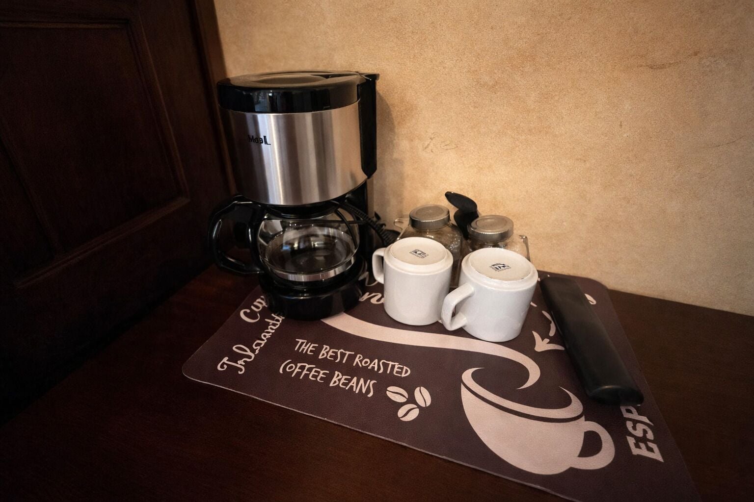 Eine Kaffeemaschine, zwei Tassen, ein Kaffeemühle und ein Beutel Kaffeebohnen auf einem Tisch.