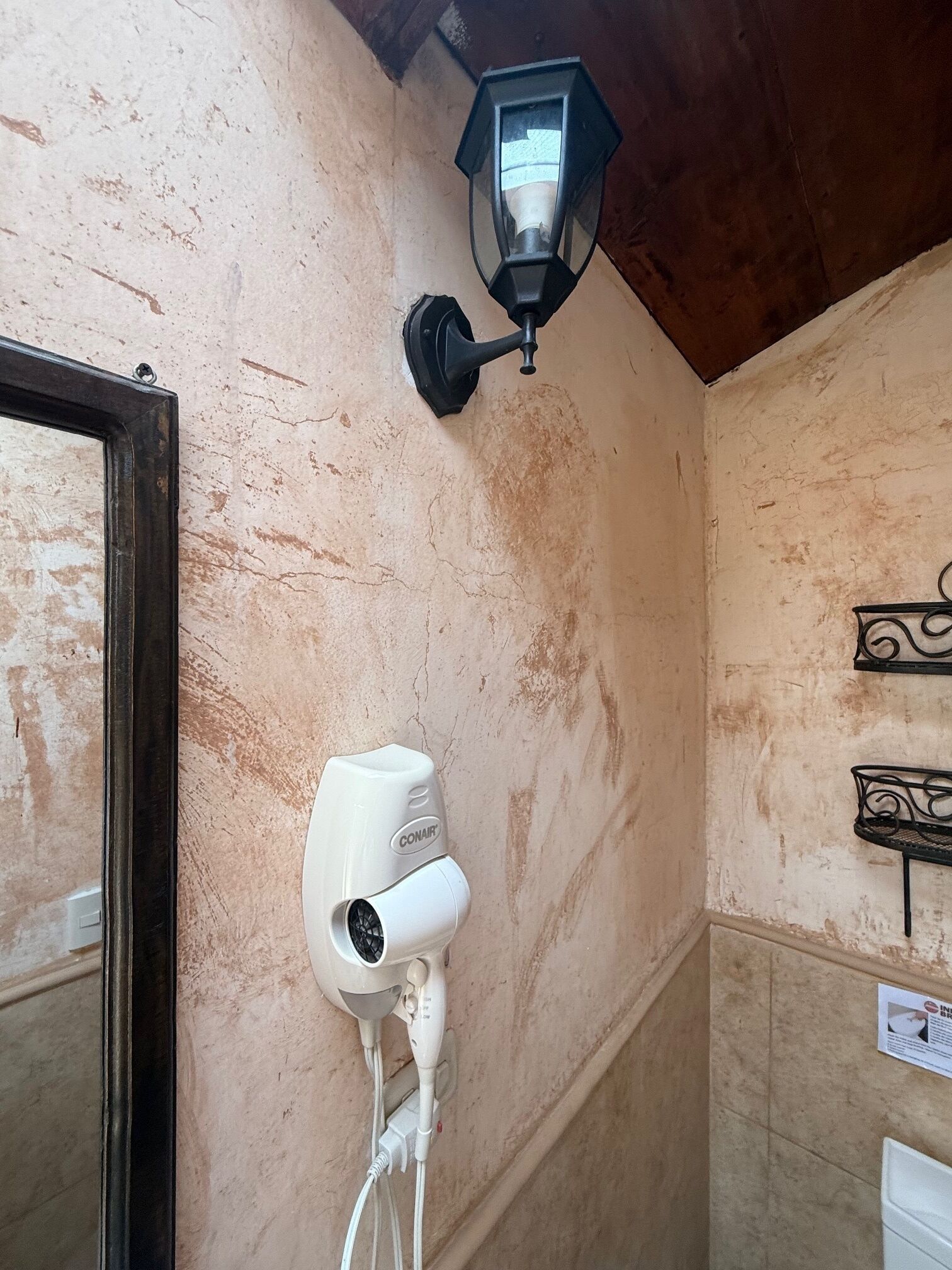 A bathroom with a hairdryer mounted on the wall, a wall-mounted light fixture, and a mirror with a wooden frame.