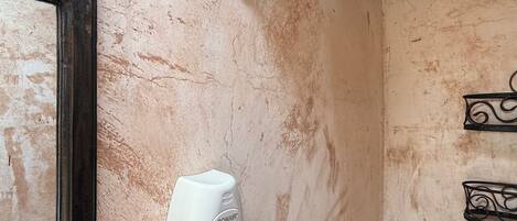A bathroom with a hairdryer mounted on the wall, a wall-mounted light fixture, and a mirror with a wooden frame.