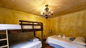 Une chambre avec des lits superposés, un lustre, un ventilateur et un petit tapis.