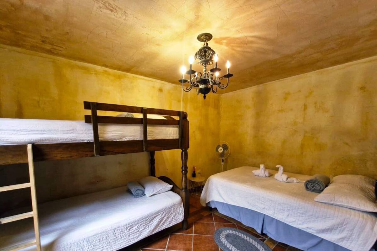 Une chambre avec des lits superposés, un lustre, un ventilateur et un petit tapis.