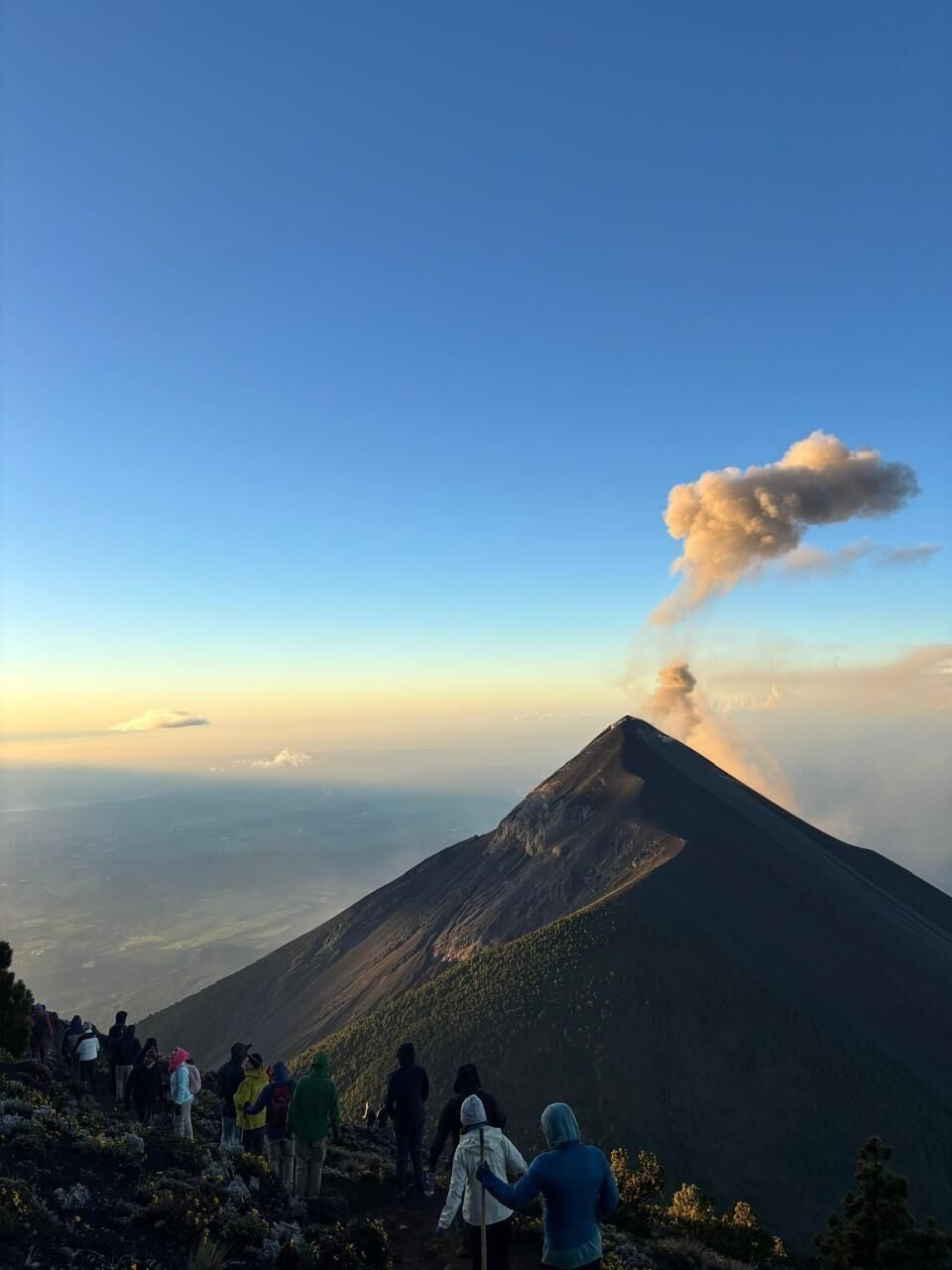 Una montagna con una colonna di fumo visibile, circondata da un gruppo di escursionisti.