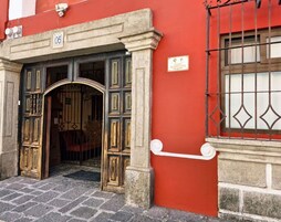 Una entrada de edificio con un arco de piedra, una verja metálica y un muro rojo.