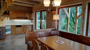 A wooden cabin interior with a kitchen, dining area, and large windows offering a view of the outdoors. - Wooden house in the middle of nature with a wonderful panorama, near to Budapest (Penc)