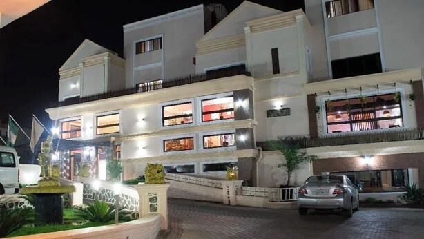 A multi-story hotel with illuminated windows and a paved driveway. - Casalinda Hotel And Resort (Abuja)