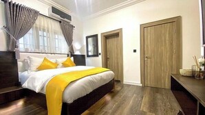A bedroom with a bed, a bedside table, a wardrobe, and a mirror. - Casalinda Hotel And Resort (Abuja)