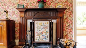 A fireplace with a floral wallpaper, a framed artwork, and a vase of flowers on top. - Country House Near Loch Earn (Lochearnhead)