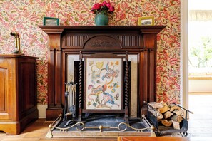 A fireplace with a floral wallpaper, a framed artwork, and a vase of flowers on top. - Country House Near Loch Earn (Lochearnhead)
