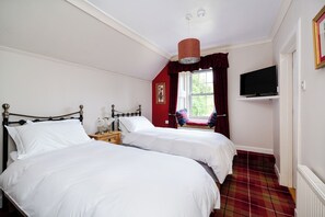 A bedroom with two beds, a television on a shelf, and a window with curtains. - Country House Near Loch Earn (Lochearnhead)