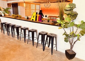 Un espace bar avec des tabourets noirs, un comptoir orné de grandes lettres et une plante en pot.