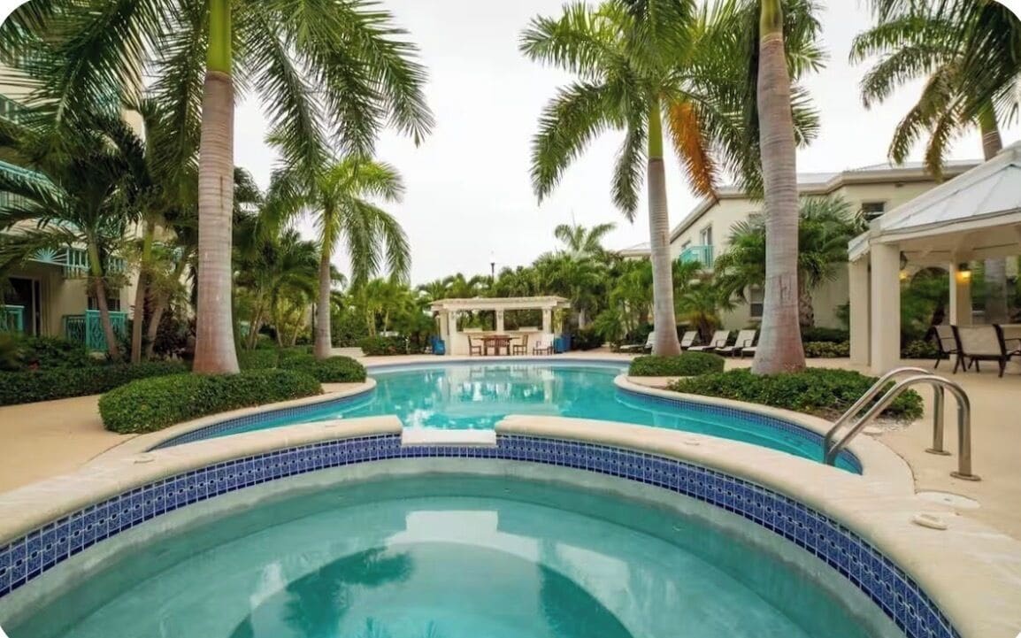 A swimming pool with palm trees, a gazebo, and lounge chairs.