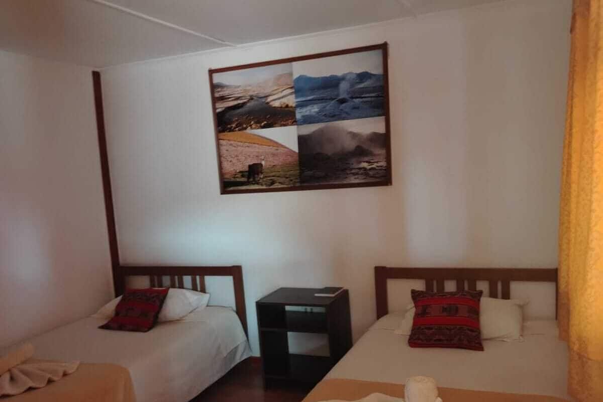 A small, cozy room with two single beds, a wooden table, and a wall-mounted picture of landscapes.