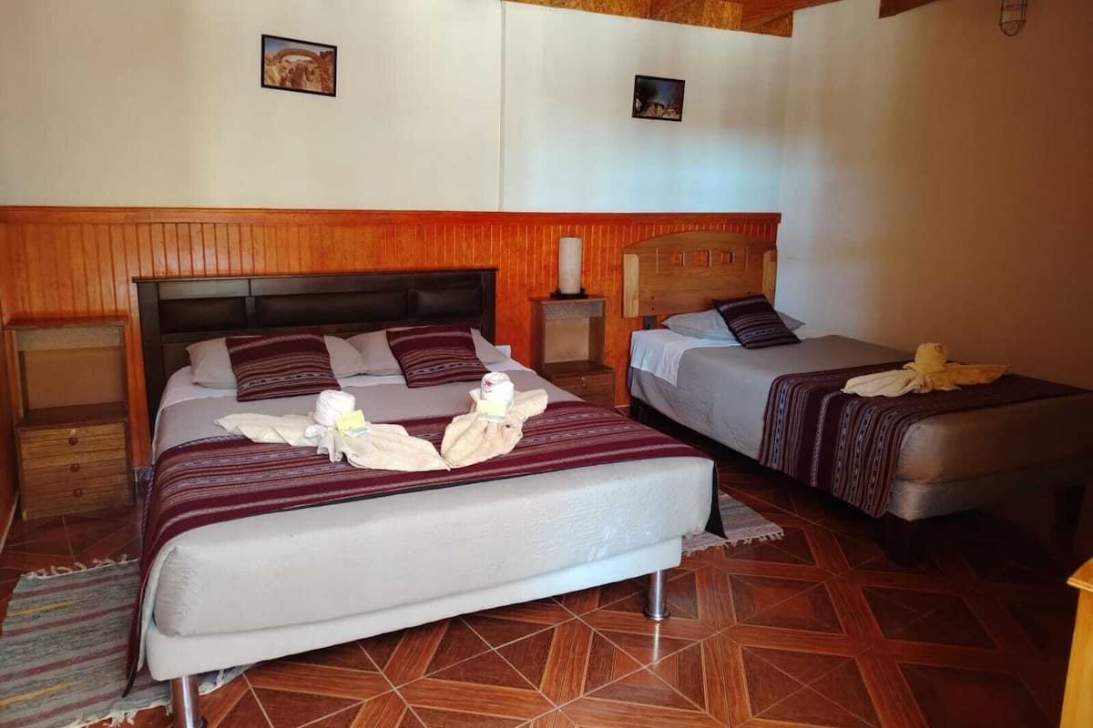 A hotel room with two beds, wooden headboards, a tiled floor, and a wooden ceiling.