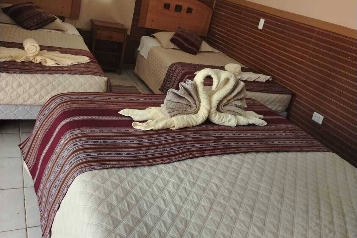 A hotel room with two beds, a wooden headboard, a wall-mounted air conditioner, and a bedside lamp.