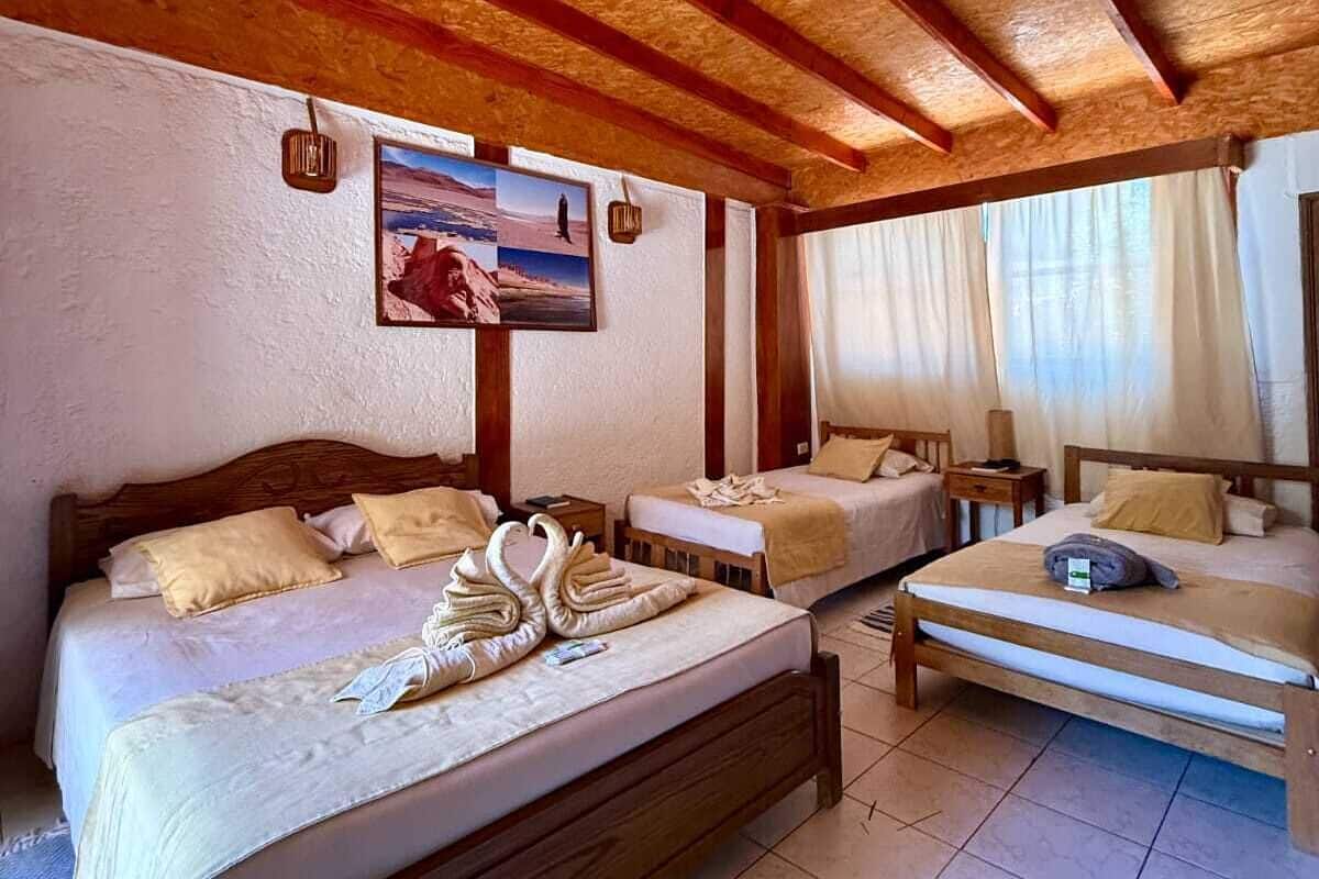 A hotel room with a wooden ceiling, a large bed, a smaller bed, a nightstand, a lamp, and a painting on the wall.