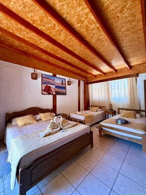 Een hotelkamer met een houten plafond, een groot bed, een kleiner bed, een nachtkastje, een lamp en een schilderij aan de muur.