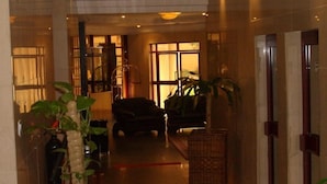 Un vestíbulo de hotel con mostrador de recepción, una zona de estar con sofá y sillones, y un ventanal que aporta luz natural.