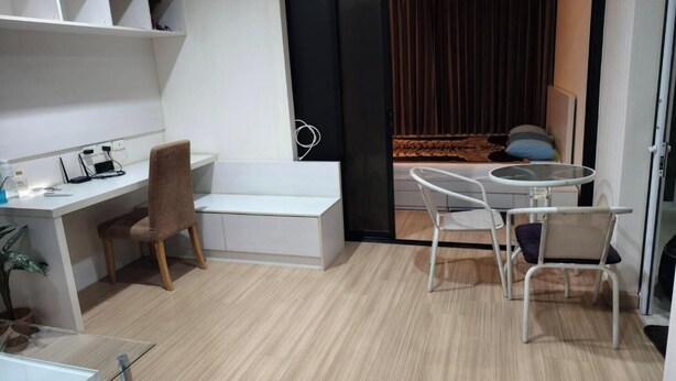 A modern room with a desk, chair, and a small table with chairs. There is a sliding door leading to a balcony with a view. - Fully furnished 1-bedroom condo with two air conditioning units in room. (Krung Thep Maha Nakhon)