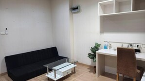 A modern living room with a black sofa, a glass coffee table, a white desk with a chair, and a potted plant. - Fully furnished 1-bedroom condo with two air conditioning units in room. (Krung Thep Maha Nakhon)