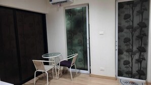 A room with a sliding glass door, a small table with two chairs, and an air conditioning unit on the ceiling. - Fully furnished 1-bedroom condo with two air conditioning units in room. (Krung Thep Maha Nakhon)