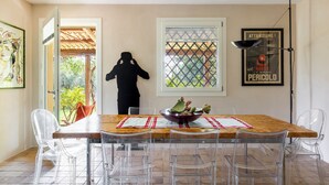 A dining area with a wooden table, clear plastic chairs, a decorative bowl, and a framed warning sign on the wall. - Villa Torre Pizzuta (Noto)