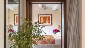 A hallway leading to a bedroom with a bed, a nightstand, a lamp, and a vase with flowers. - Villa Torre Pizzuta (Noto)