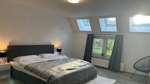 A bedroom with a bed, two bedside tables with lamps, a chair, and skylights. - ME LIVING - Holiday apartment - 2 bathrooms (Lemgo)