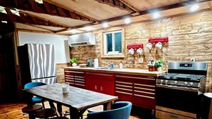 A rustic kitchen with wooden beams, a stainless steel refrigerator, a stove, and a dining area with a wooden table and blue chairs. - Stay in this historic Automotive-themed huge Apt. Located in charming Whitingham (Whitingham)