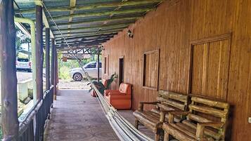 A covered outdoor area with a wooden bench, a hammock, and a car parked in the background.
